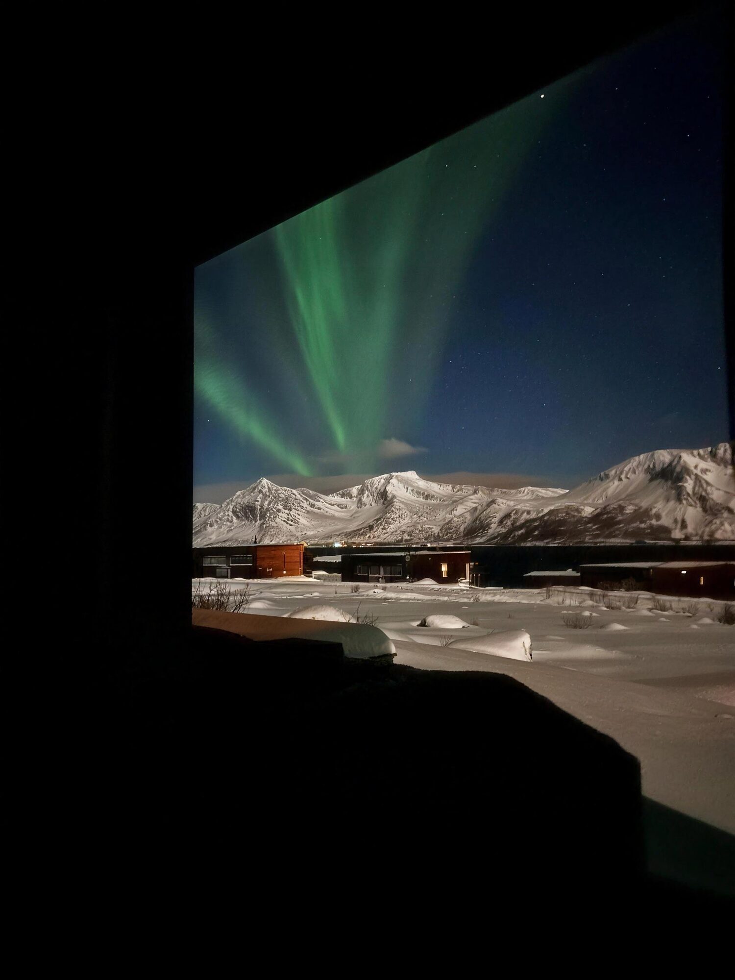 The northern lights over white mountains, seen through a window from a dark room